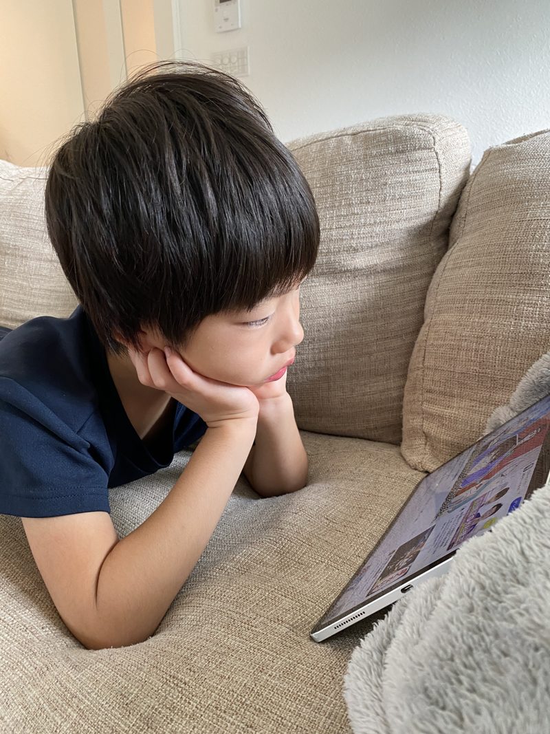 ソファで頬杖をついてタブレットを見る子どもの写真