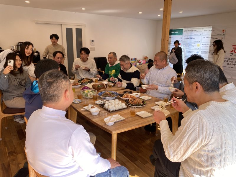 昼のリビングで、大人たちが大きな食卓を囲んで食べている写真